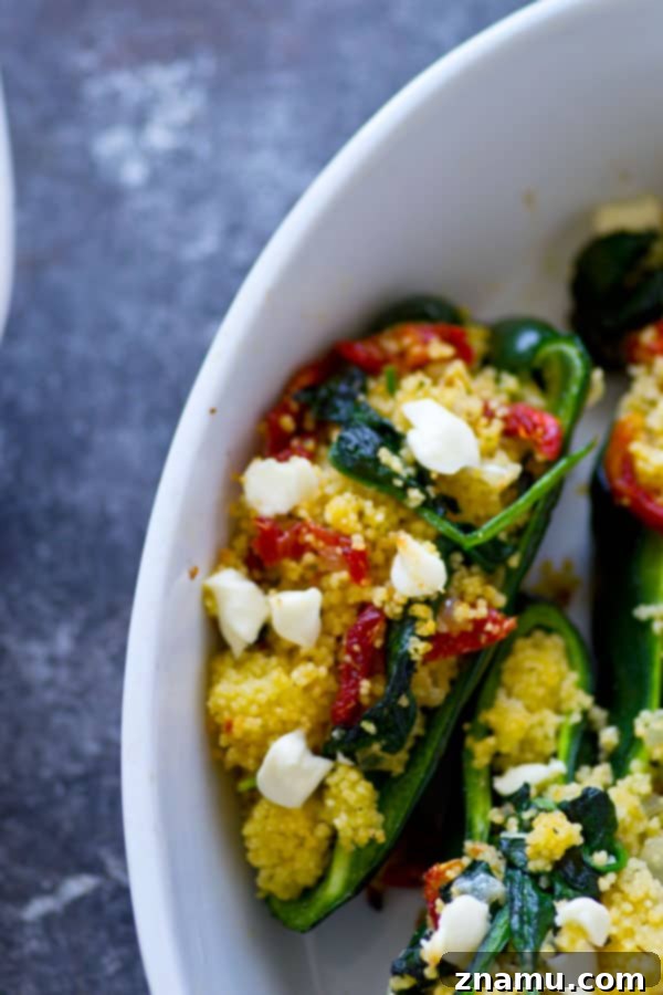 Close-up of a partially cut stuffed poblano pepper revealing goat cheese and couscous filling