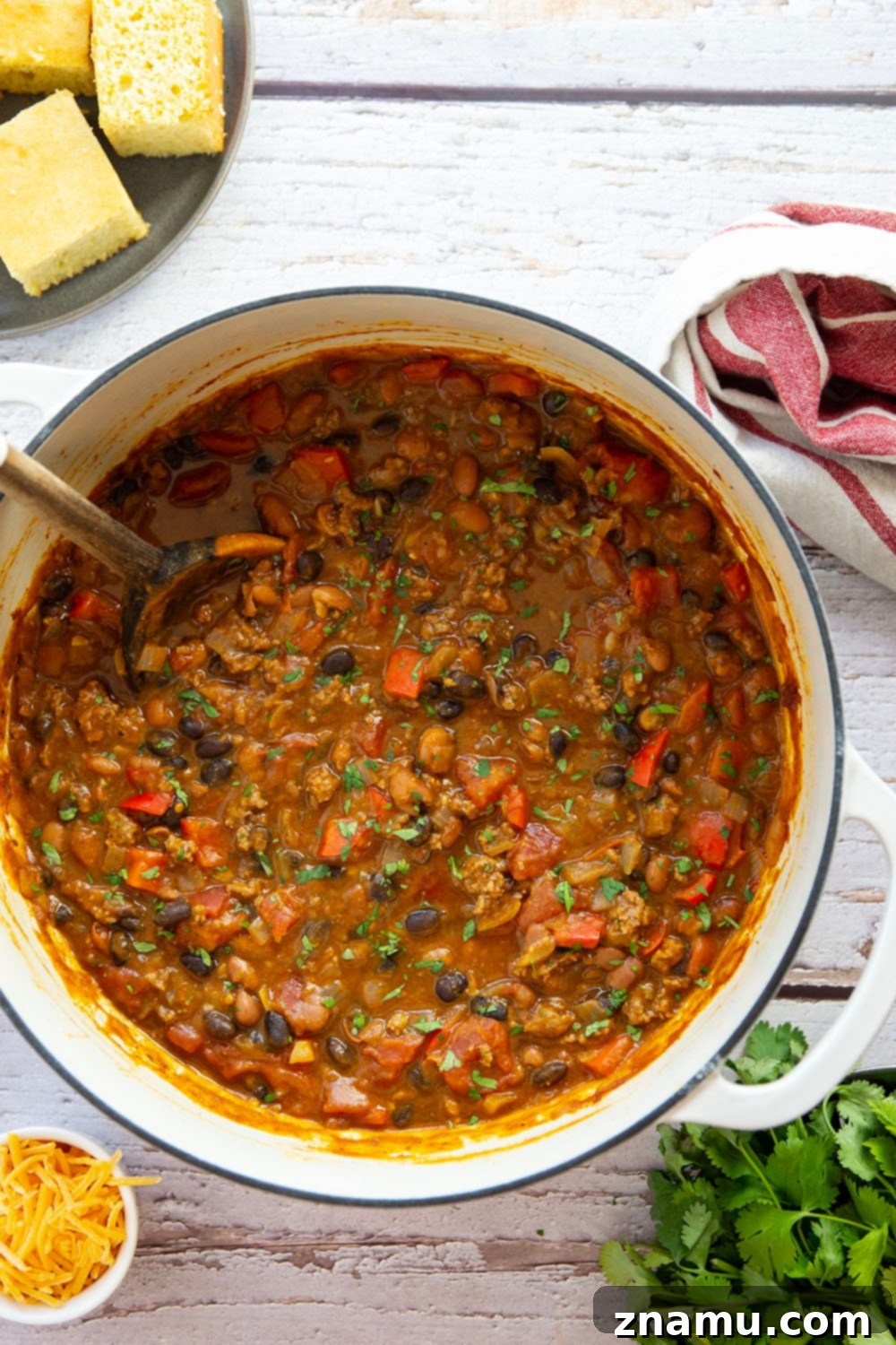Harvest Gold Pumpkin Chili 3 An overhead view of a large pot brimming with rich, orange-hued pumpkin chili, showing off the hearty ground beef, various beans, and colorful vegetables simmering.