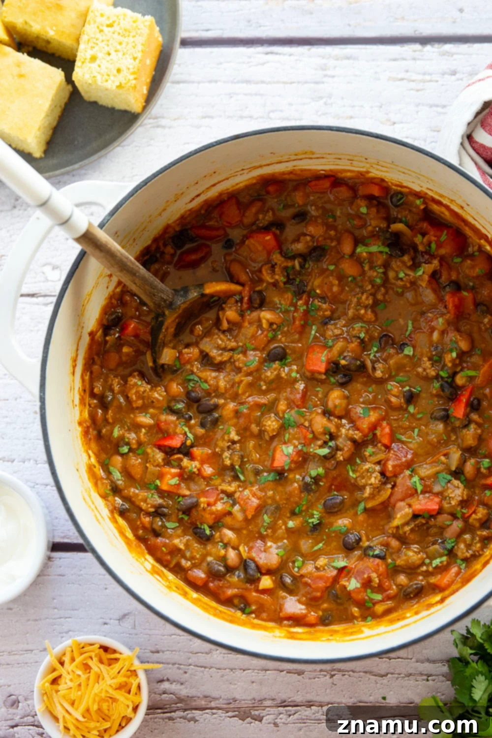 Harvest Gold Pumpkin Chili 5 A large wooden spoon stirring a rich, orange-tinted pumpkin chili in a rustic Dutch oven, showcasing the blend of ground beef, beans, and vegetables.