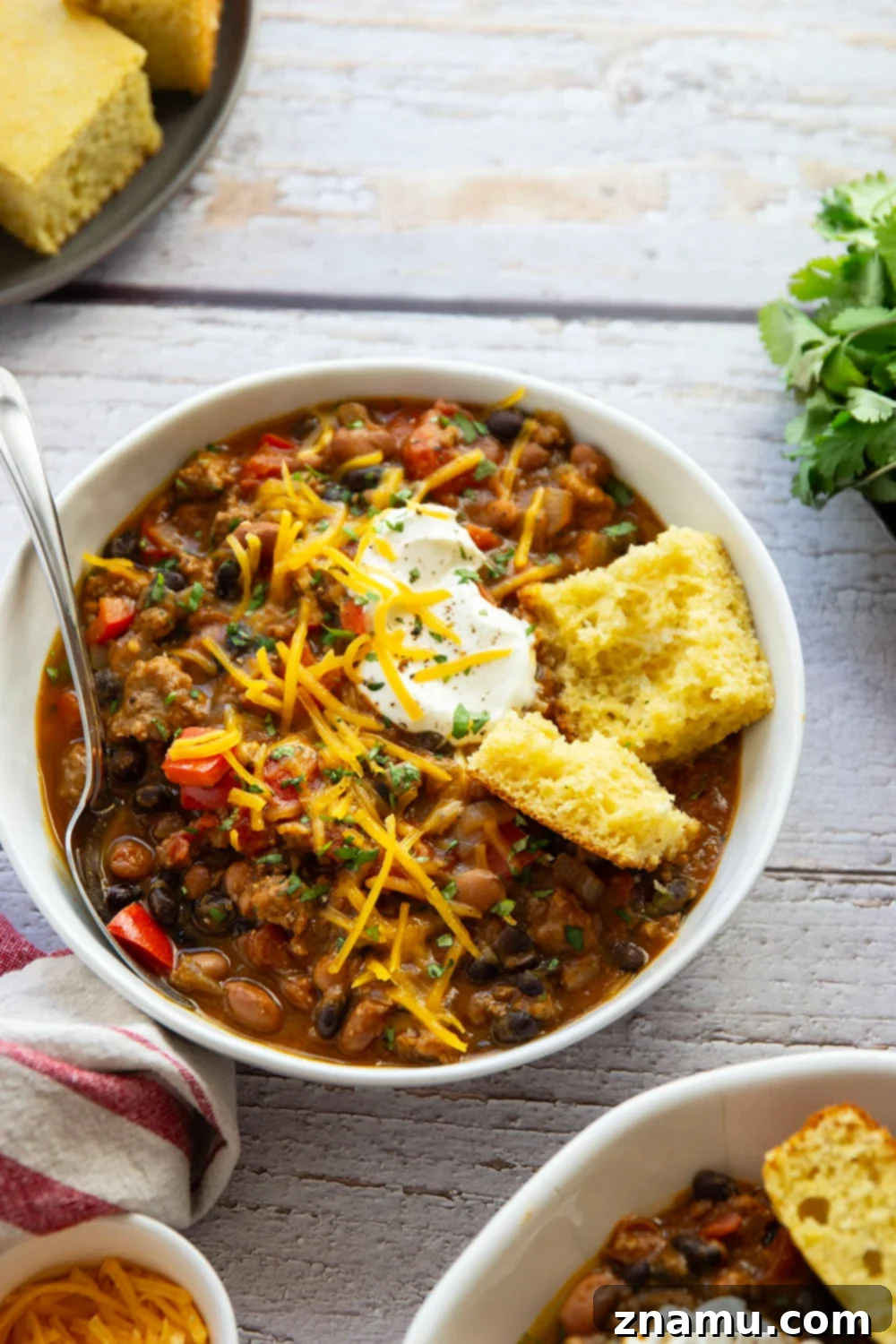 Harvest Gold Pumpkin Chili 6 A vibrant bowl of pumpkin chili, garnished with a generous dollop of sour cream, fresh green onions, and a sprinkle of cheese, placed on a cozy patterned napkin.