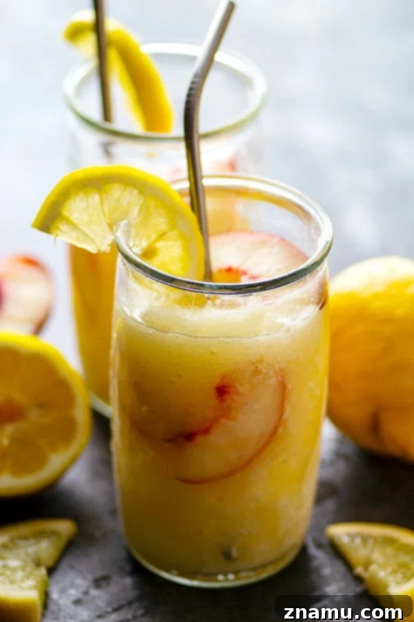 Spiked Peach Lemonade Slush 2 Two glasses of frosty Frozen Peach Rum Lemonade Slushies, garnished with fresh peach slices and mint.