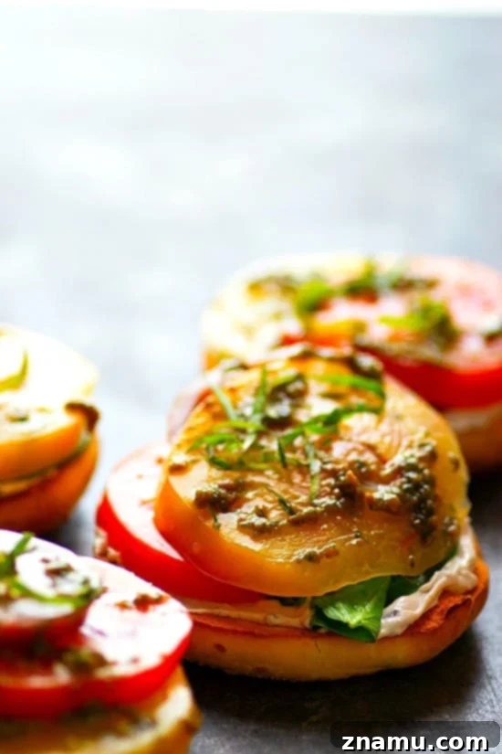 Artisan Heirloom Tomato and Goat Cheese Bagel Toasts 2 A close-up of a beautifully assembled open-faced heirloom tomato and goat cheese bagel sandwich, showcasing vibrant red and orange tomato slices, creamy white goat cheese, and fresh green basil leaves on a toasted bagel half. The image captures the juicy texture of the tomatoes and the rich spread of the cheese, inviting viewers to savor this fresh, summery treat.