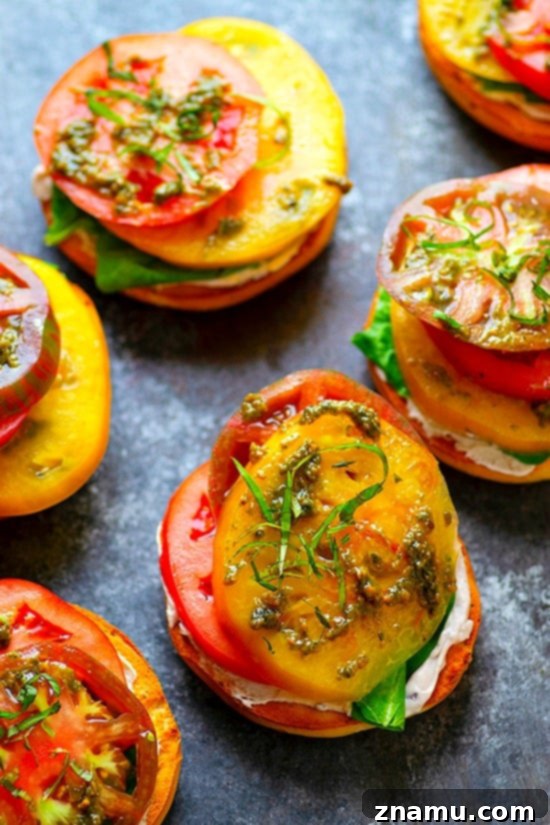 Artisan Heirloom Tomato and Goat Cheese Bagel Toasts 3 Two open-faced heirloom tomato and goat cheese bagel halves on a wooden cutting board, garnished with fresh basil. The angle highlights the thick slices of juicy heirloom tomatoes, the generous layer of goat cheese, and the golden-brown crust of the toasted bagels, inviting enjoyment.