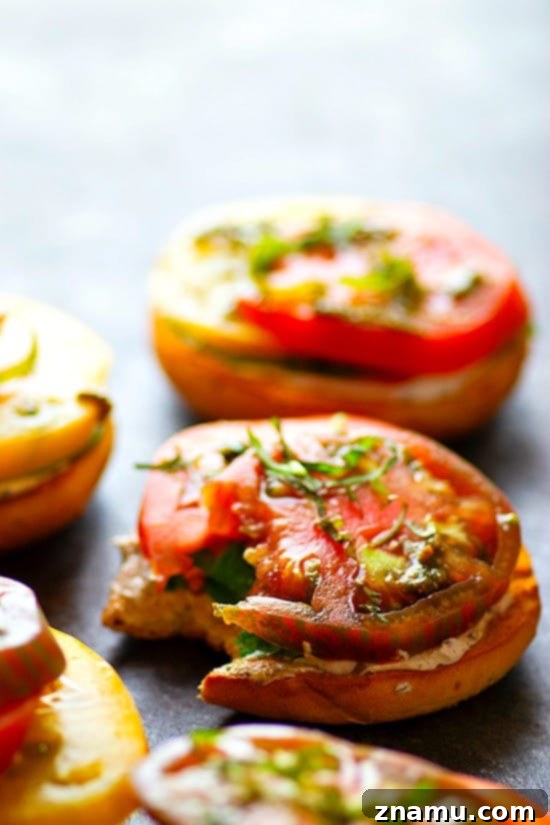 Artisan Heirloom Tomato and Goat Cheese Bagel Toasts 5 A vibrant open-faced bagel sandwich featuring a thick layer of creamy goat cheese, generously topped with slices of colorful heirloom tomatoes and fresh basil. The image showcases the abundant, fresh ingredients on a rustic wooden surface, embodying a healthy and delicious summer meal.