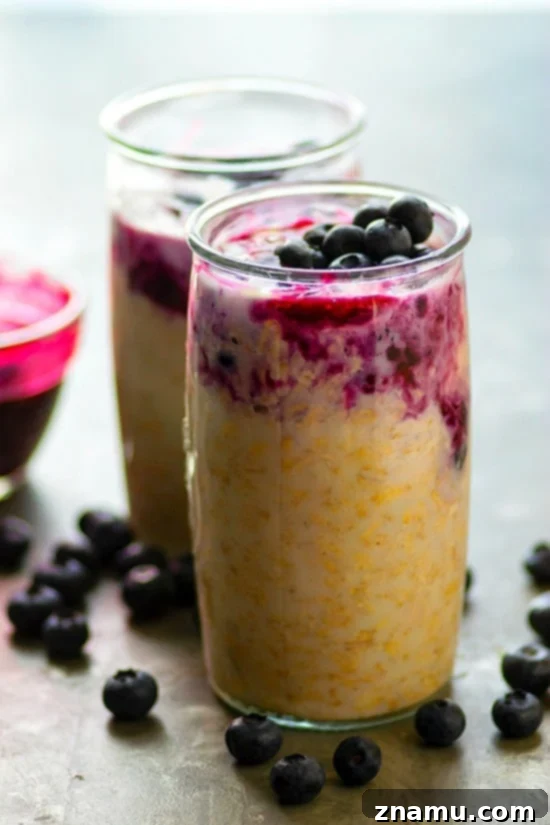 Layers of blueberry pie and cheesecake swirled into oats in a glass jar
