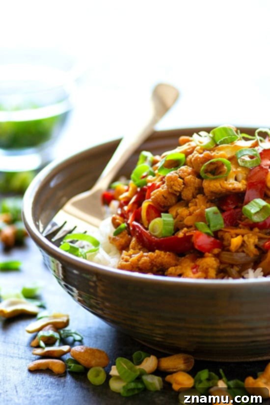 A serving bowl filled with Miso Sweet Pepper Cashew Cauliflower Stir-Fry and steamed rice, garnished with green onions and cashews