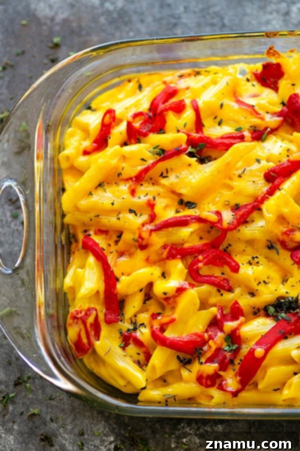 Pumpkin and Roasted Red Pepper Mac & Cheese 5 Baked Pumpkin Roasted Red Pepper Mac 'n' Cheese - A close-up, top-down view of a serving spoon scooping a generous portion of the cheesy, vibrant mac and cheese, showing stringy melted cheese.