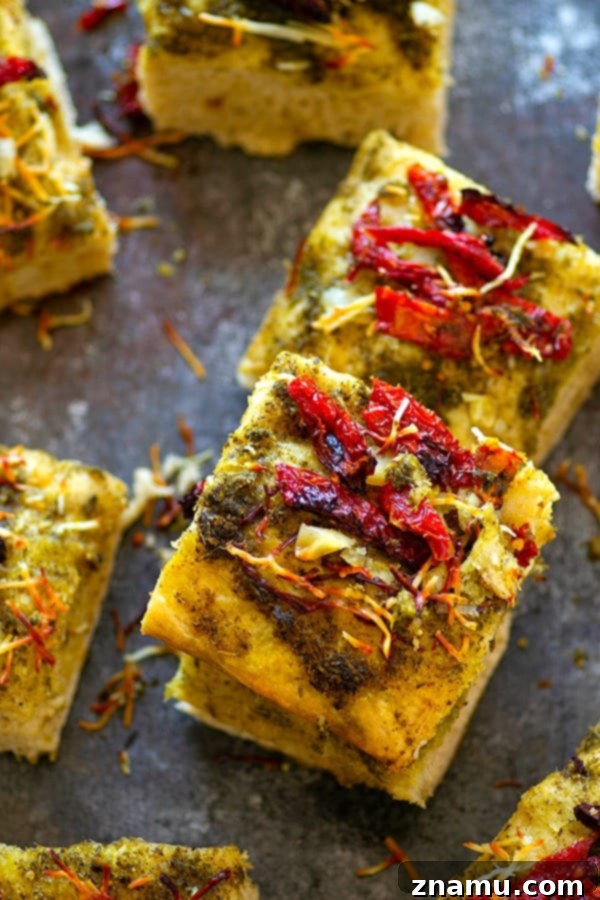 Close-up of fluffy focaccia bread topped with roasted garlic, sun-dried tomatoes, and pesto