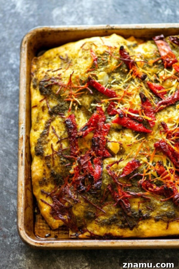 A large sheet of freshly baked focaccia, golden brown with dimples and abundant toppings