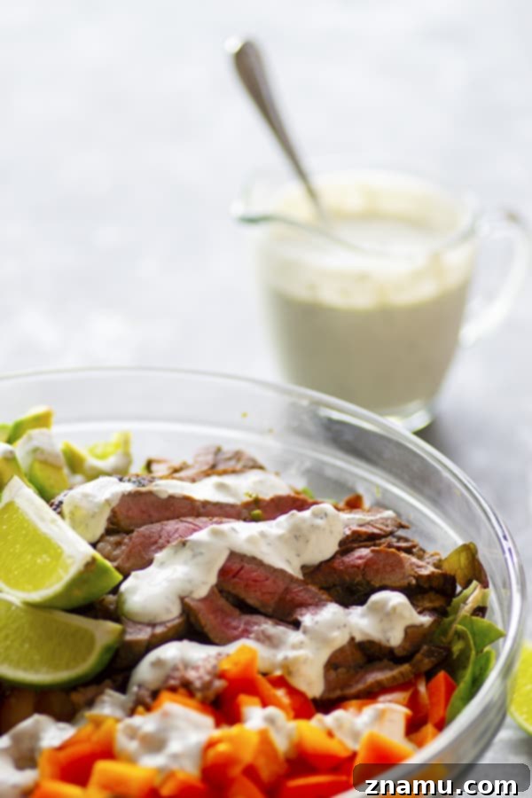 Hearty Carne Asada Bowls with Bold Bleu Cheese 5 A fully assembled Carne Asada Steak Salad Bowl, showcasing thin slices of steak over mixed greens, colorful vegetables, and a generous drizzle of creamy bleu cheese dressing.