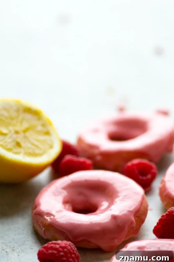 Zesty Lemon Sour Cream Doughnuts with Raspberry Glaze 5 A hand dipping a baked lemon donut into a bowl of vibrant, naturally pink raspberry glaze.