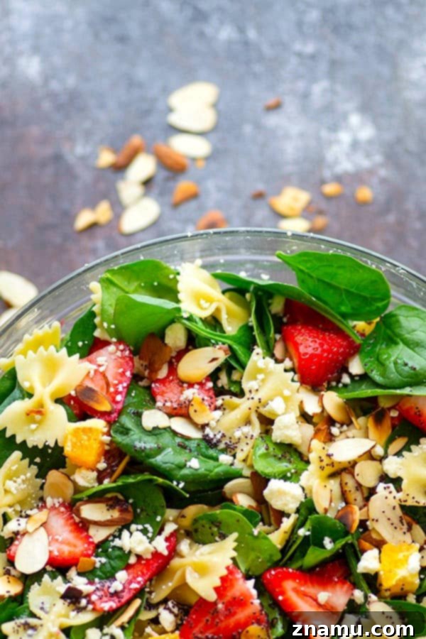 Close-up shot of the Strawberry Poppyseed Spinach Pasta Salad, highlighting the texture of the bowtie pasta, the crispness of the spinach, and the vibrant hues of the strawberries and feta. The tangy poppyseed dressing coats each component beautifully, promising a burst of flavor.