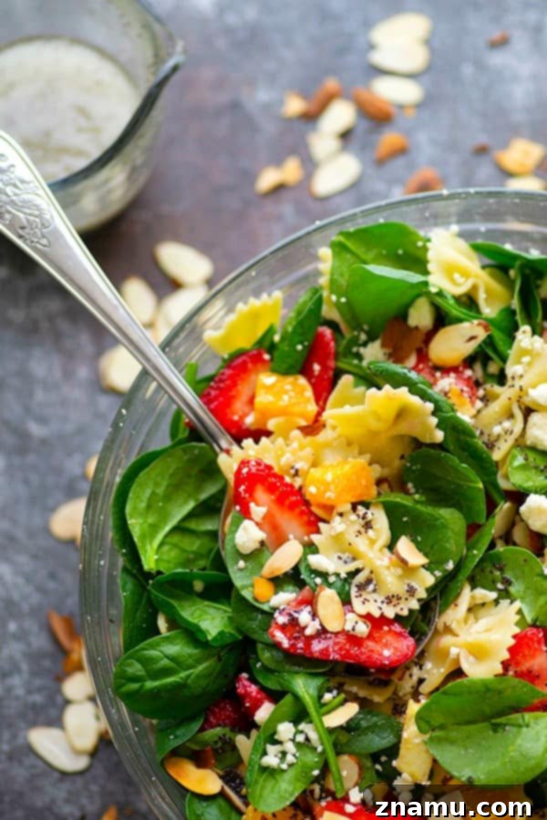A closer view of the assembled Strawberry Poppyseed Spinach Pasta Salad, showcasing the intricate mix of ingredients. The bowtie pasta, fresh spinach, bright red strawberries, and creamy feta are generously coated in a rich, homemade poppyseed dressing, promising a delightful culinary experience.