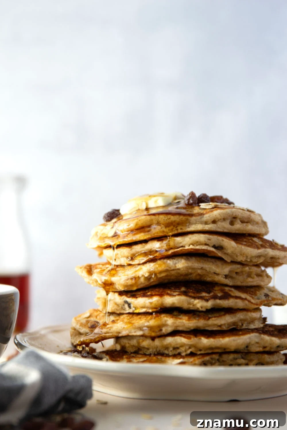 Wholesome Oat and Raisin Pancakes 2 A tall stack of golden brown oatmeal raisin pancakes, garnished with plump raisins and a drizzle of maple syrup, reflecting a cozy morning scene.