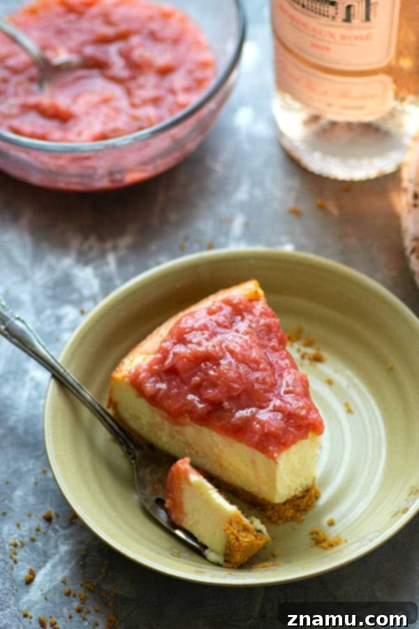 White Chocolate Rosé Rhubarb Serenade 5 A beautifully sliced piece of Rhubarb Rosé White Chocolate Cheesecake on a fork, showing the distinct layers of crunchy crust, creamy filling, and vibrant rhubarb topping.