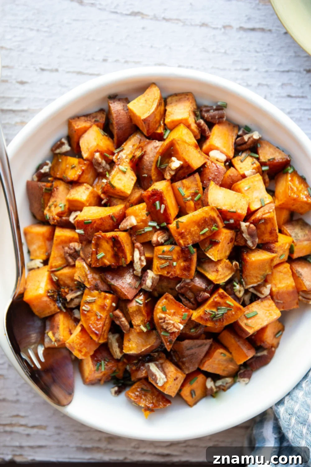 Roasted Sweet Potatoes with Maple and Rosemary 4 Cooked rosemary roasted sweet potatoes with maple syrup and pecans in a serving bowl, garnished with more fresh rosemary.