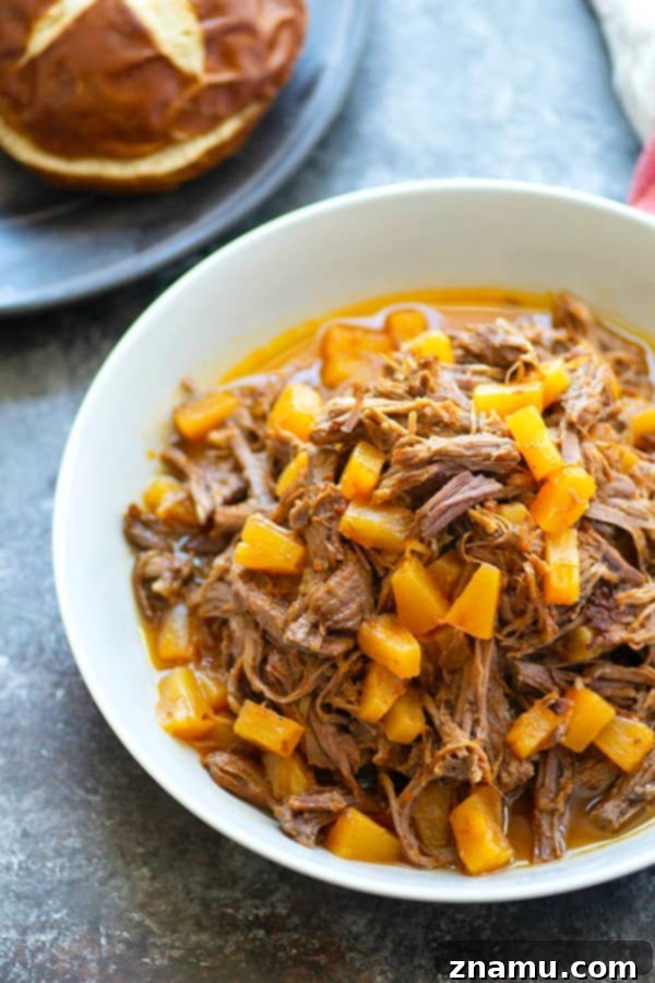 Tropical Instant Pot BBQ Beef Sandwiches 4 A plate featuring a fully assembled Instant Pot Pineapple BBQ Beef Sandwich with fresh ingredients.