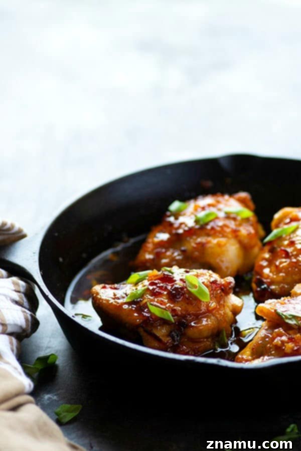 Three honey chipotle chicken thighs baked in a cast-iron skillet, coated in a rich, dark orange sticky sauce and garnished with fresh green onions, ready for serving.