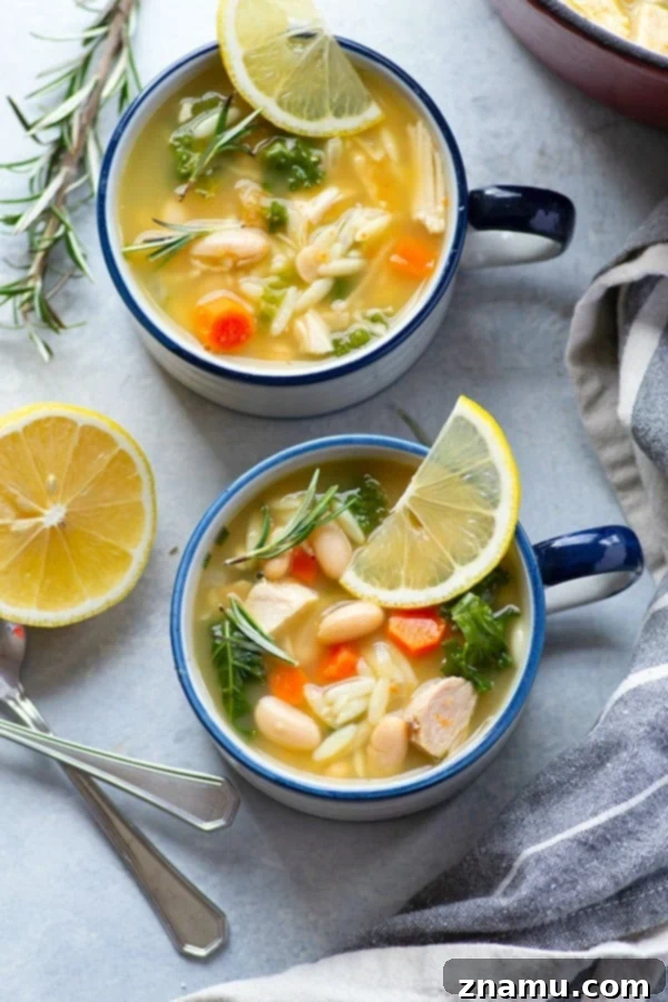 A steaming bowl of hearty Turkey Orzo Kale White Bean Soup, garnished with fresh rosemary and lemon.