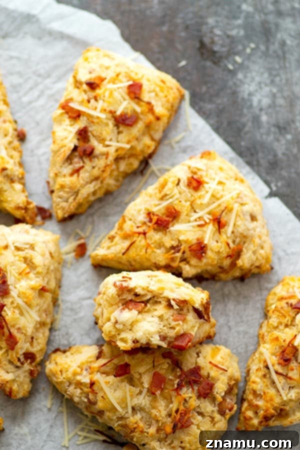 Three golden-brown Asiago Caramelized Onion Bacon Scones arranged on a wooden board, showcasing their delicious texture and savory ingredients.