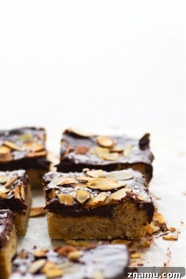 Decadent Chocolate Ganache Almond Sugar Cookie Bars 2 Rich chocolate ganache almond sugar cookie bars on a white platter, sprinkled with flaky sea salt and toasted almonds. Perfect for holiday baking.