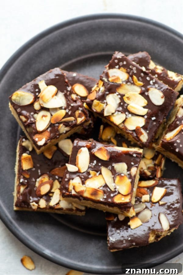 Decadent Chocolate Ganache Almond Sugar Cookie Bars 4 A slice of almond sugar cookie bar with thick chocolate ganache and sea salt on a white marble surface, highlighting its rich texture.