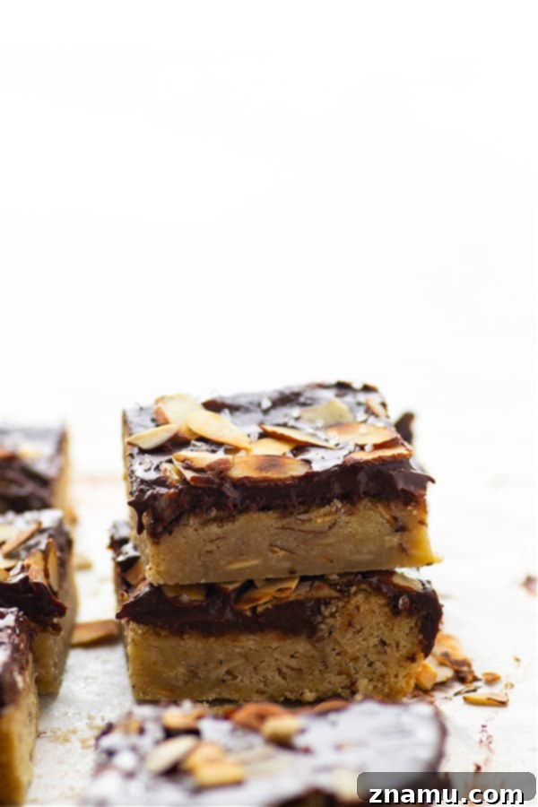 Decadent Chocolate Ganache Almond Sugar Cookie Bars 5 Stacked chocolate ganache almond sugar cookie bars on a rustic wooden tray, ready for holiday serving. Emphasizes the rich layers.