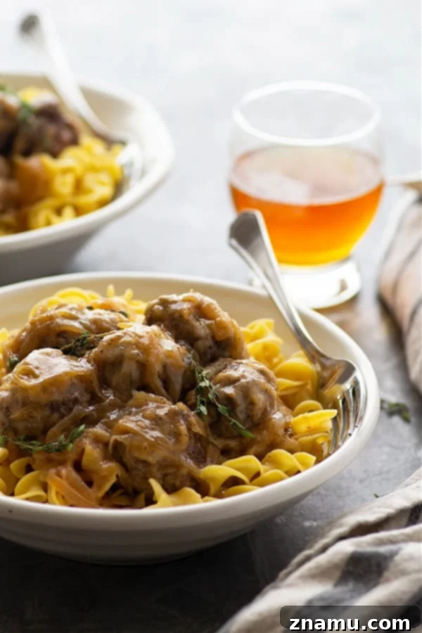 A close-up of French Onion Soup Meatballs nestled in a rich sauce, topped with melted Swiss cheese, ready to be served over pasta.
