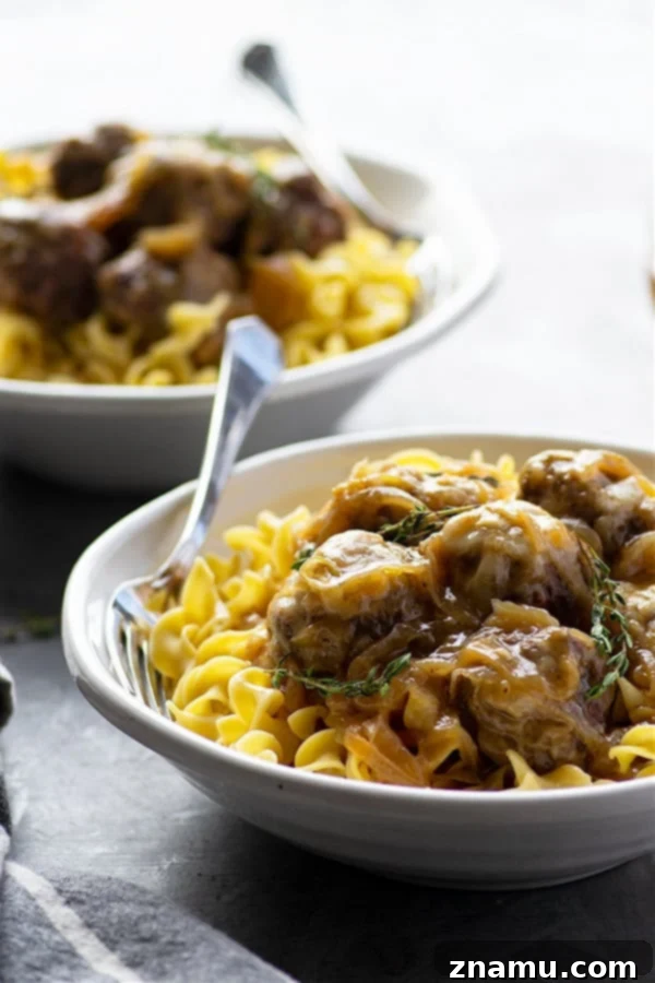 A bowl of Instant Pot French Onion Soup Meatballs, topped with a generous amount of melted Swiss cheese, with a spoon ready to serve.