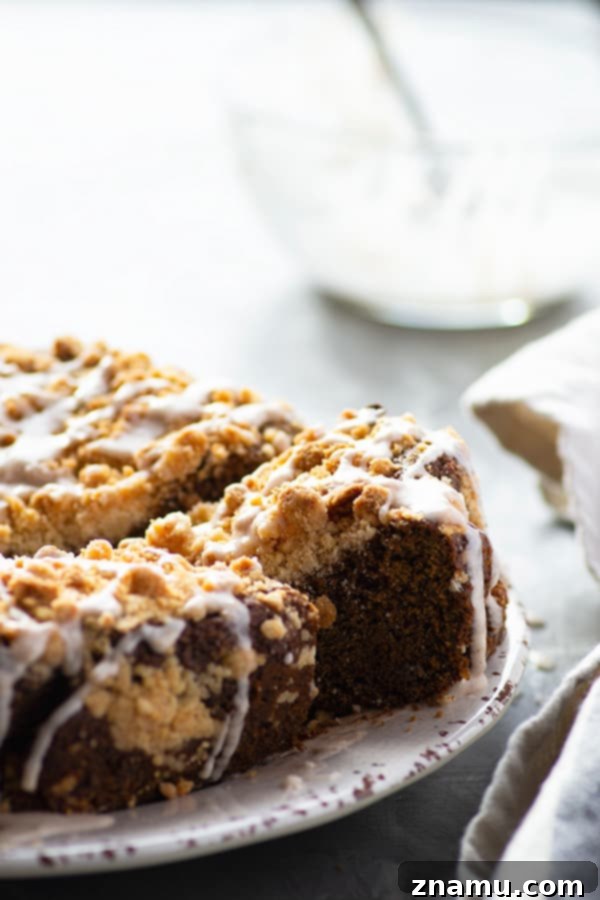 Brown Butter Gingerbread Crumb Coffee Cake 2 A whole round browned butter gingerbread coffee cake with streusel topping and white glaze, set on a rustic white surface with a festive background, perfect for holiday brunch.