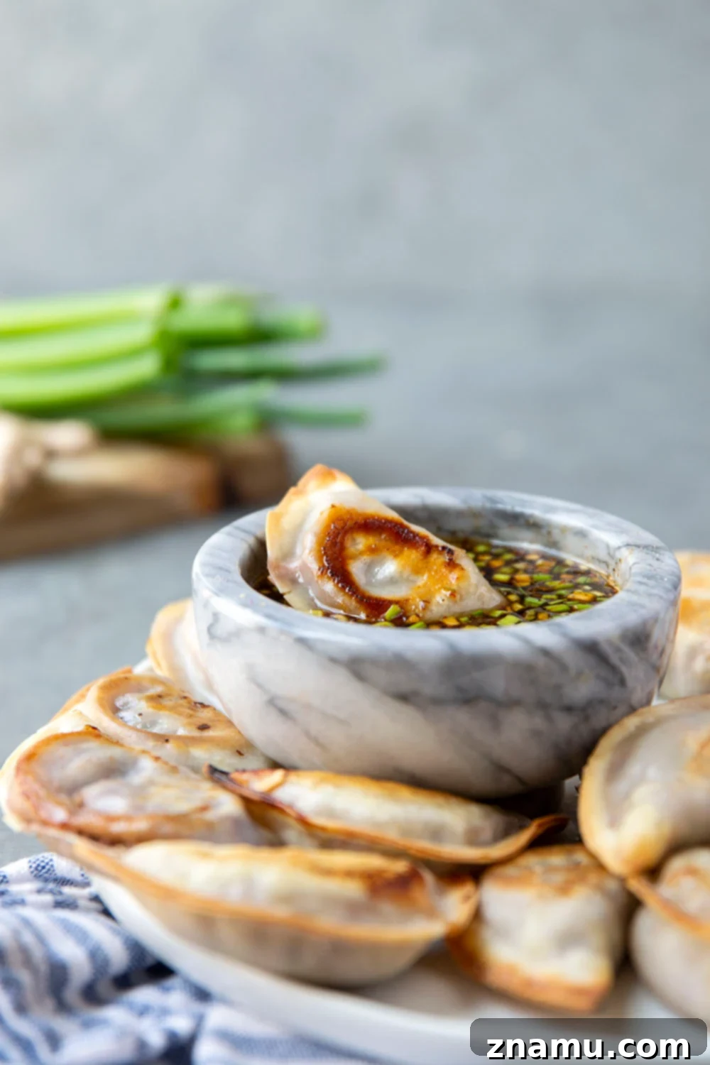 Crispy Sheet Pan Spicy Chicken Potstickers with a bowl of ginger dipping sauce, garnished with green onions.