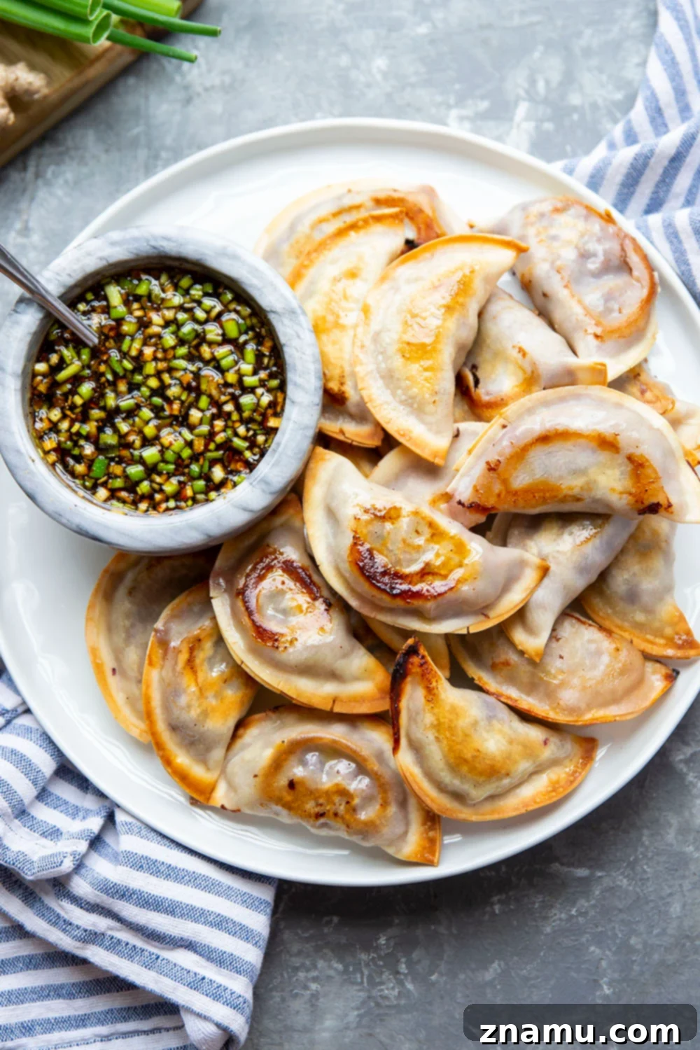 A close-up of a perfectly baked spicy chicken potsticker being dipped into the ginger sauce.
