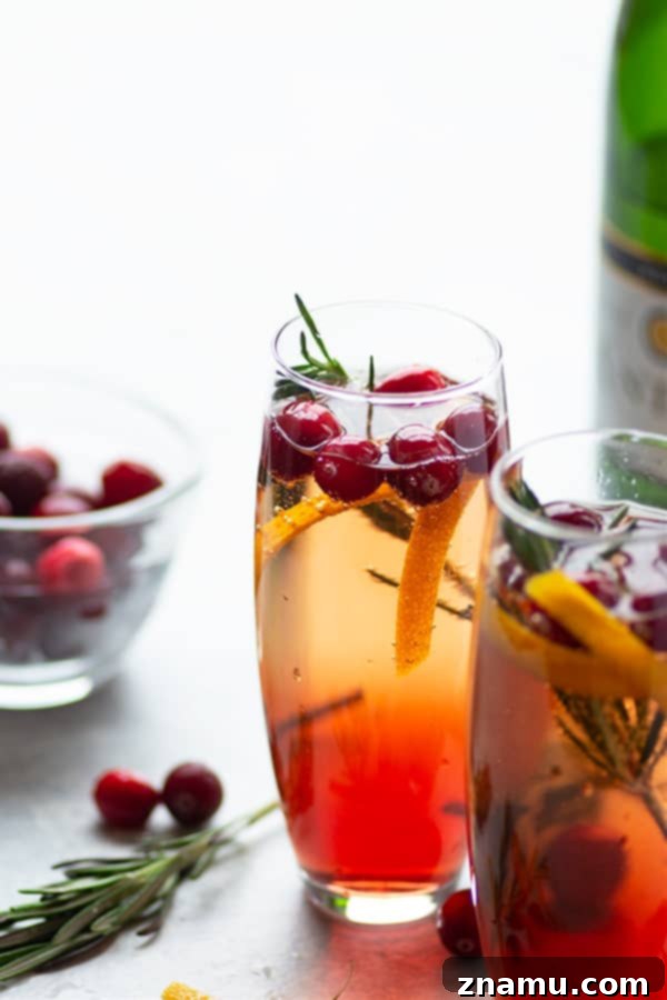 Poinsettia cocktail in a flute, garnished with fresh cranberries and rosemary, set against a festive background.