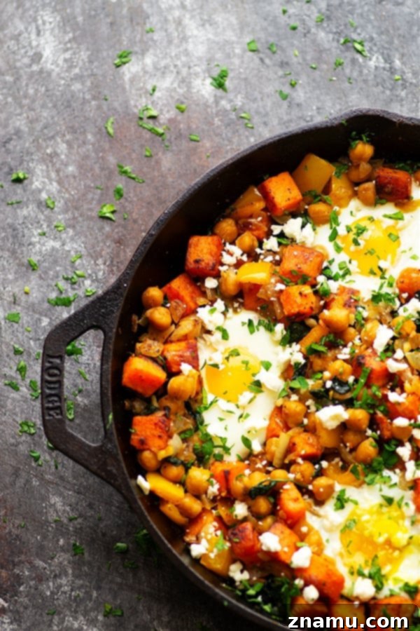 Another enticing shot of a sweet potato breakfast hash in a rustic cast iron skillet, showcasing the golden-brown edges of the sweet potatoes, vibrant green spinach, and perfectly cooked eggs with runny yolks, promising a delicious and nutritious meal.
