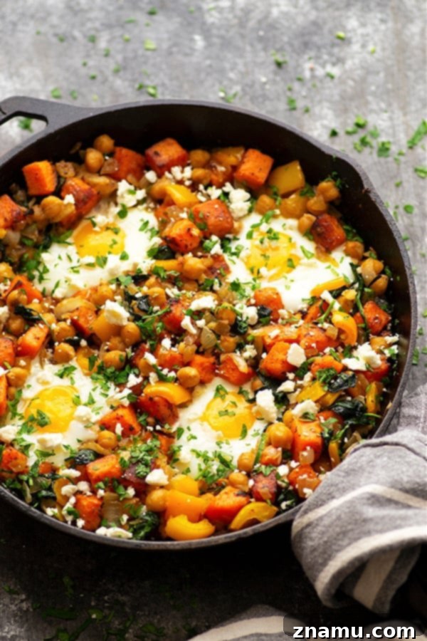 A delicious sweet potato breakfast hash with a baked egg, topped with fresh parsley and feta cheese, served in a cast iron skillet. Highlight of healthy and protein-rich breakfast.