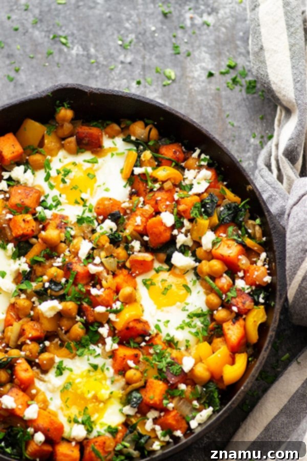 A close-up of a beautifully baked sweet potato breakfast hash with four sunny-side-up eggs, garnished with fresh parsley and feta cheese. The vibrant colors and textures make it an appealing and healthy meal.