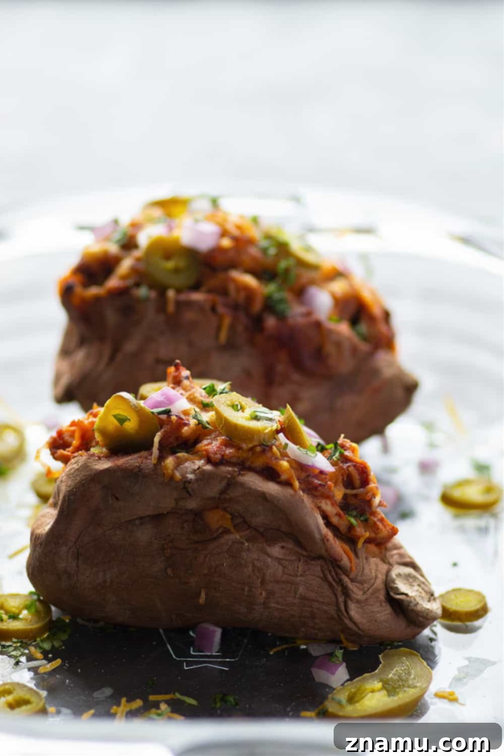 Smoky BBQ Chicken Loaded Sweet Potatoes 4 An overhead shot of a freshly baked sweet potato overflowing with barbecue pulled chicken, melted cheese, and a colorful array of fresh toppings like cilantro and red onion, presented on a rustic board.