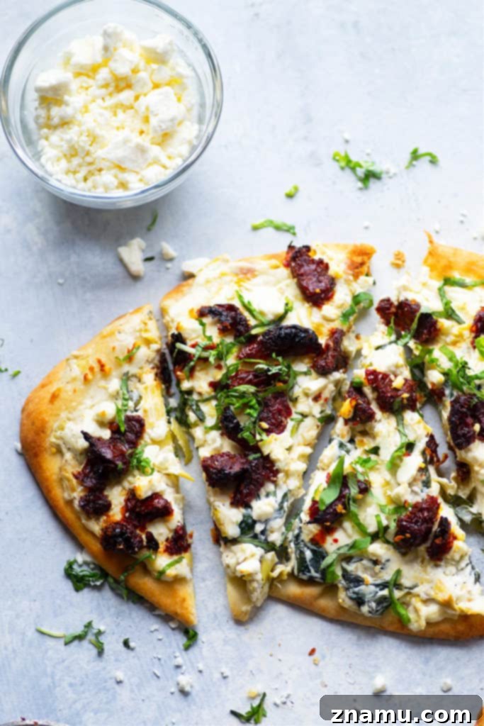 Vibrant Spinach Artichoke Flatbread with Sun-Kissed Tomatoes and Feta 5 A slice of spinach artichoke flatbread with sun-dried tomatoes and feta, showcasing its delicious layers.