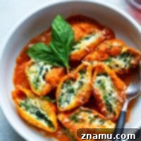 A close-up of baked spinach ricotta stuffed shells with basil vodka sauce, garnished with fresh basil.