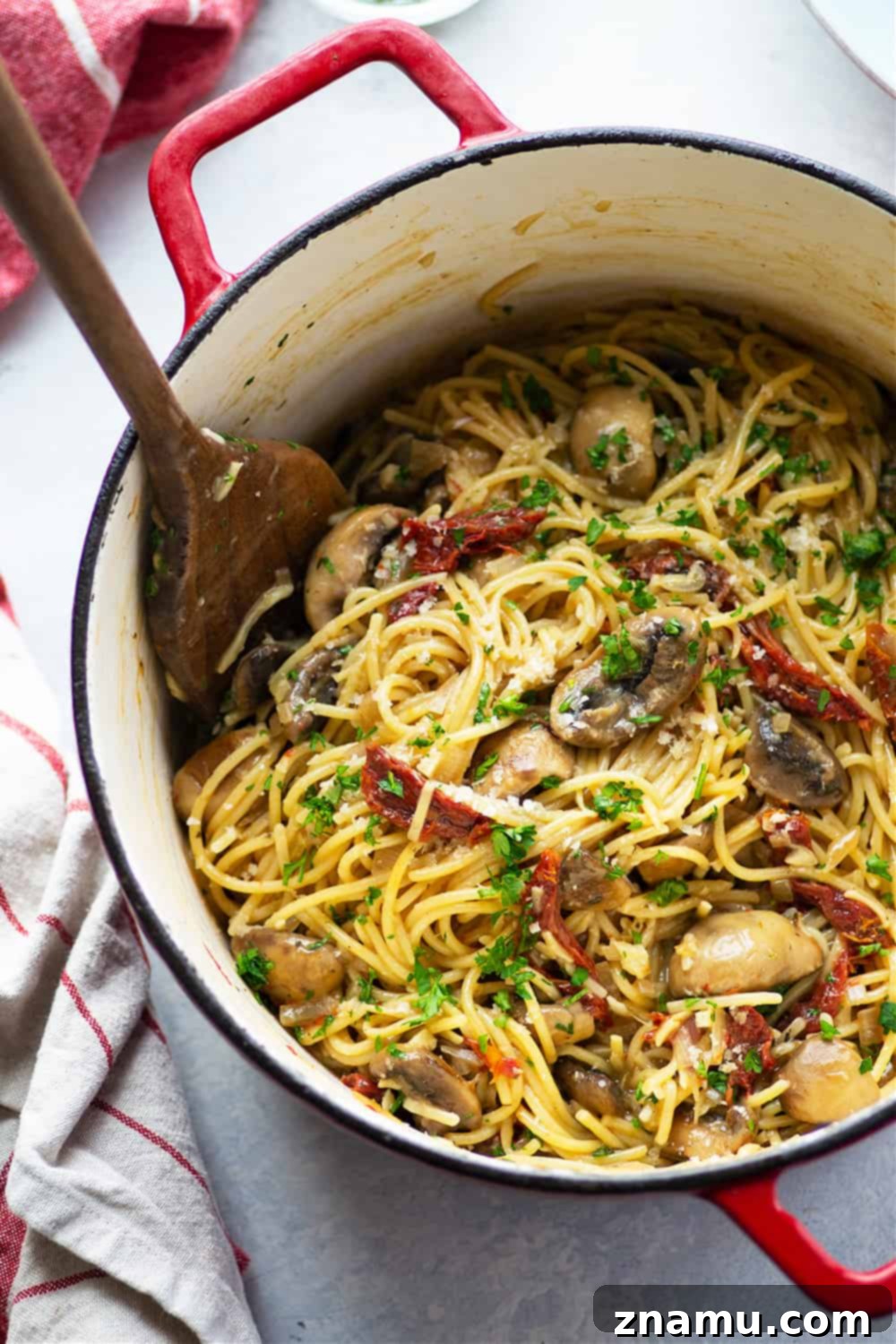 Sundried Tomato & Mushroom Carbonara 4 Overhead shot of a large pan filled with freshly cooked Mushroom Carbonara, featuring glossy spaghetti, an abundance of mushrooms and sun-dried tomatoes, and a creamy sauce. Garnished with fresh green herbs, it looks ready to serve.