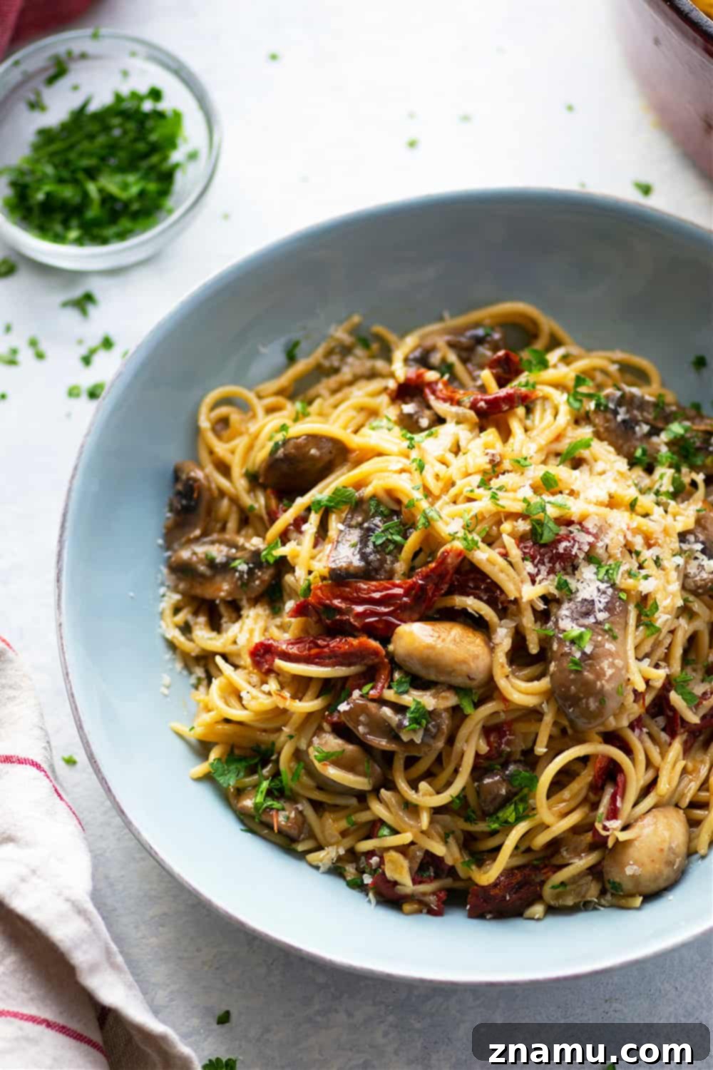 Sundried Tomato & Mushroom Carbonara 5 A serving of Mushroom Carbonara in a bowl, garnished with freshly grated Parmesan cheese and a sprig of parsley. The rich, golden sauce, visible mushrooms, and tomatoes make for an irresistible presentation.