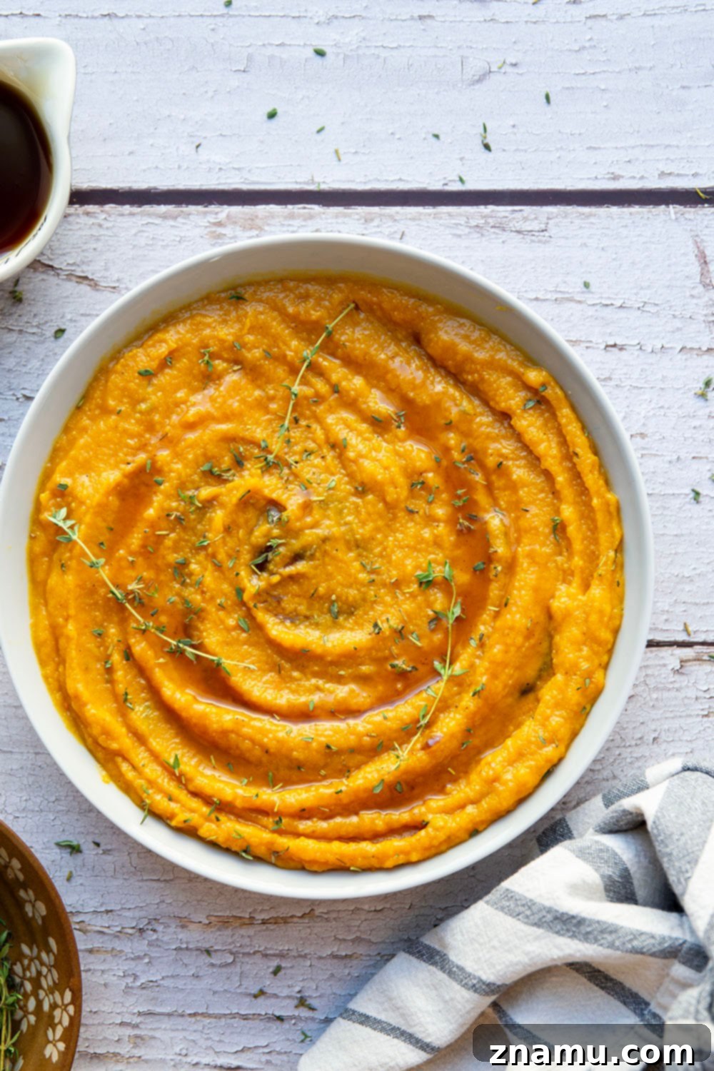 Creamy Maple Butternut Mash 2 Close-up of creamy maple mashed butternut squash garnished with fresh thyme leaves in a white bowl.