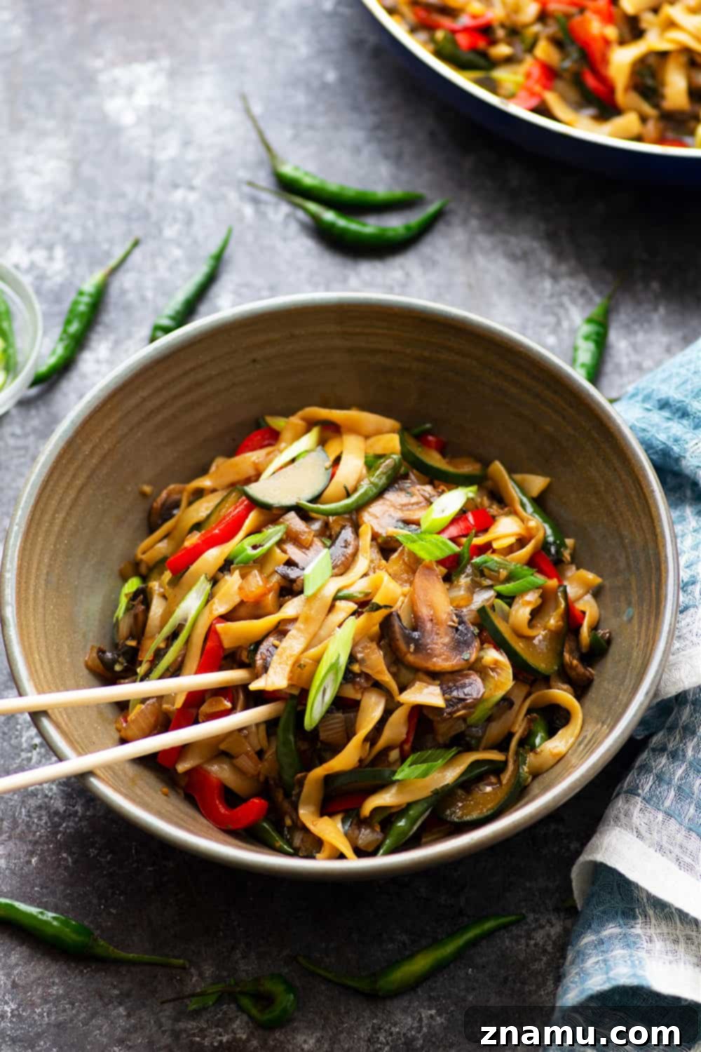 Spicy Vegan Thai Drunken Noodles 4 A bowl of freshly prepared Vegan Thai Drunken Noodles (Pad Kee Mao) garnished with fresh Thai basil leaves, chili slices, and green onions. The vibrant green of the basil contrasts beautifully with the dark, saucy noodles and colorful vegetables, emphasizing the freshness of the ingredients.