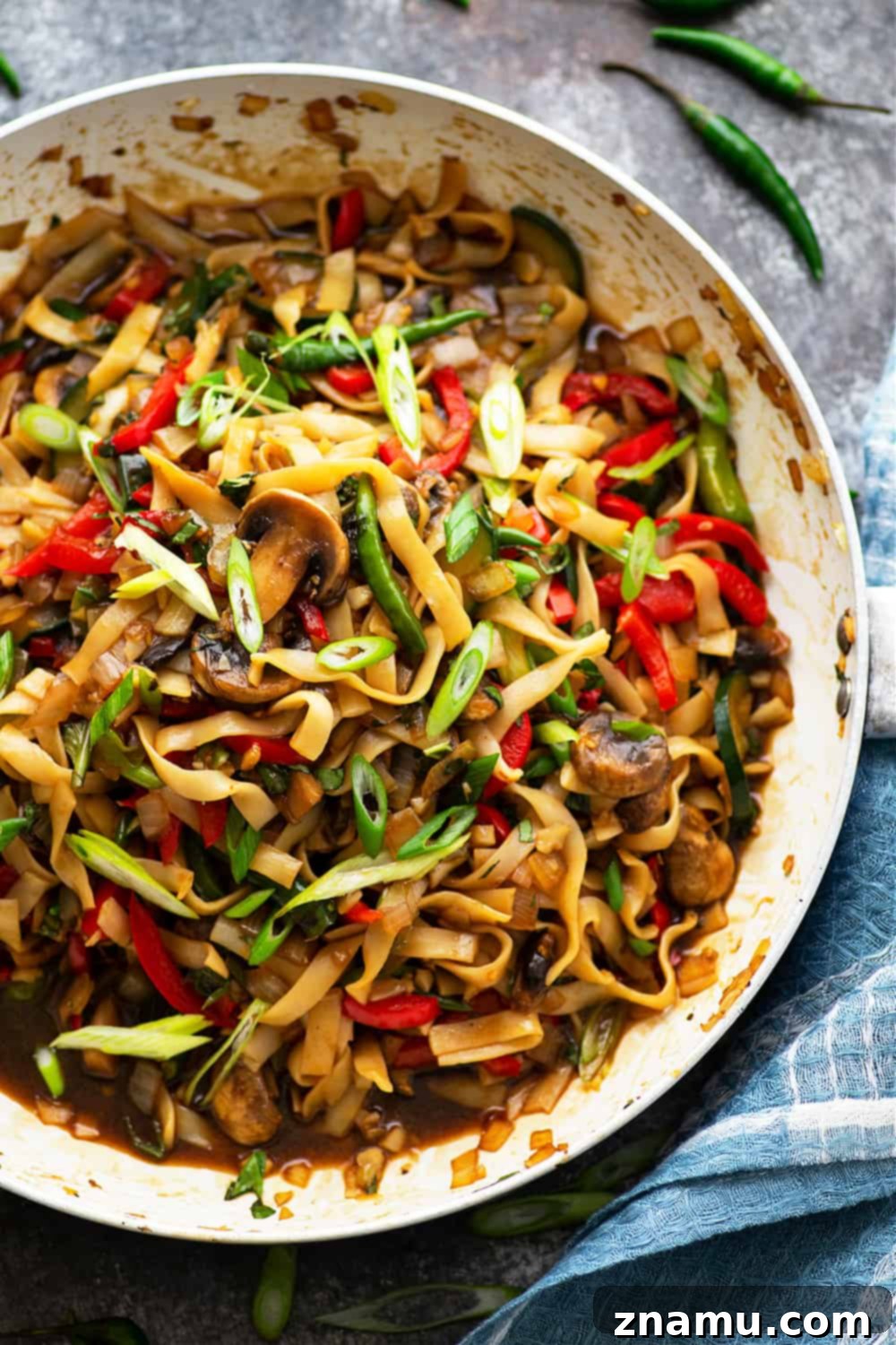 Spicy Vegan Thai Drunken Noodles 5 A close-up shot of a single serving of Vegan Thai Drunken Noodles in a white bowl, garnished with fresh Thai basil and chili flakes. The focus is on the rich texture of the noodles and the colorful, well-coated vegetables, inviting the viewer to taste.
