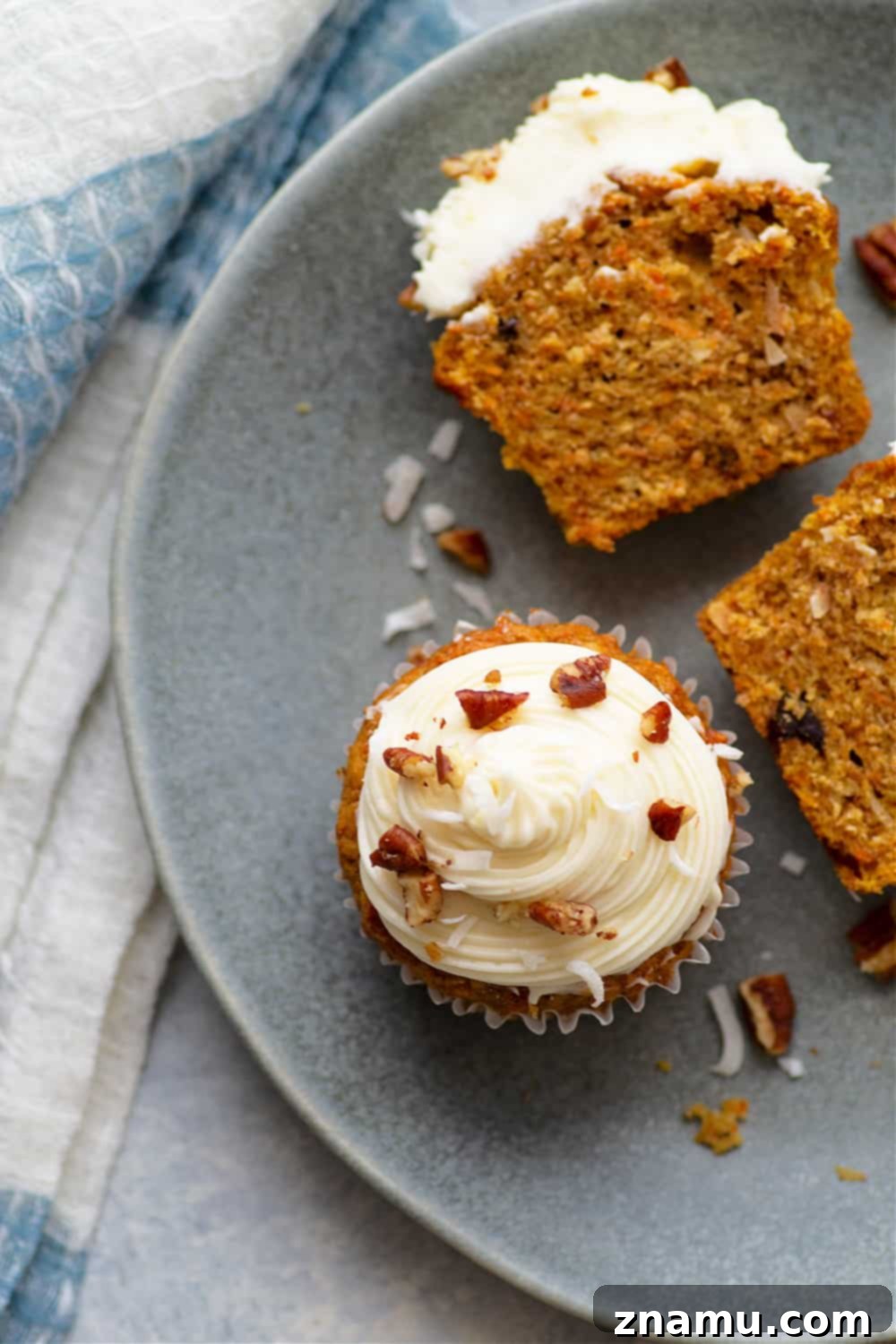 Close-up of a Coconut Carrot Cake Cupcake revealing its moist interior, nuts, coconut, and cream cheese frosting.