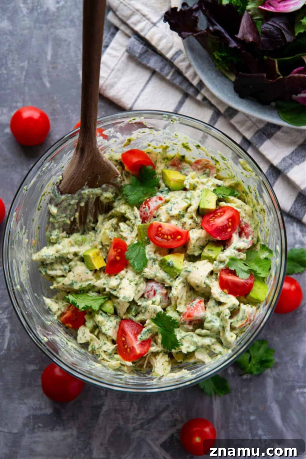Emerald Goddess Chicken Salad 5 A serving of Green Goddess Chicken Salad in a bowl, surrounded by fresh ingredients and a slice of bread.