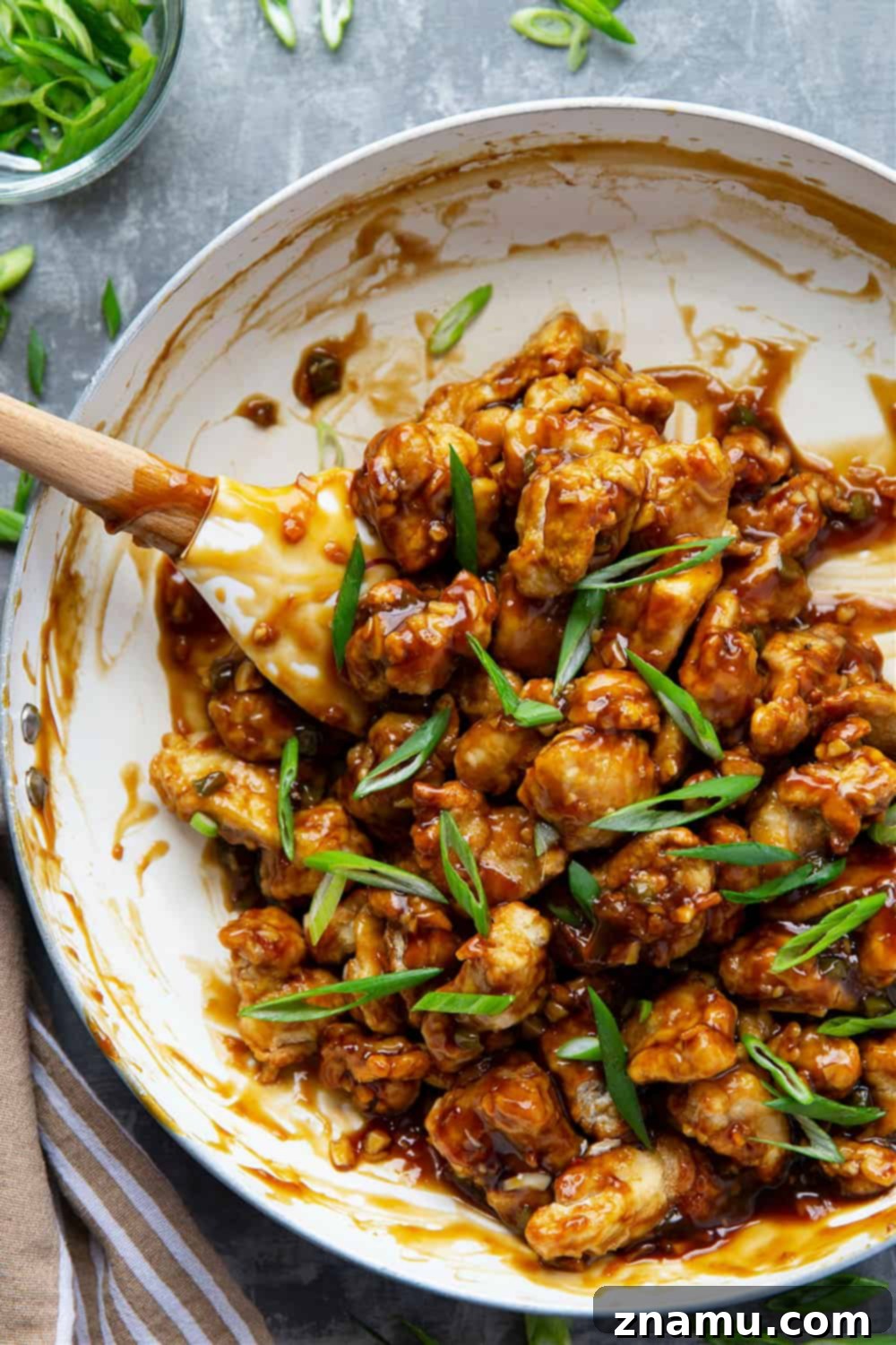 Zesty & Crispy Air Fryer Orange Chicken 4 A serving of homemade air fryer orange chicken in a bowl, drizzled with glossy orange sauce and topped with fresh green onions.