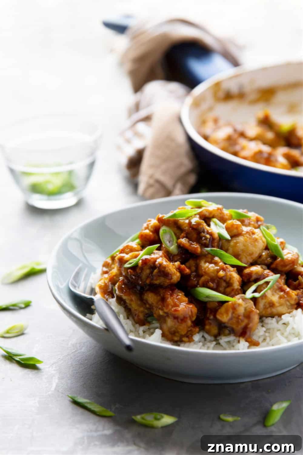 Zesty & Crispy Air Fryer Orange Chicken 5 A bowl of glossy air fryer orange chicken served over rice, with a sprinkle of chopped green onions and a side of oranges.