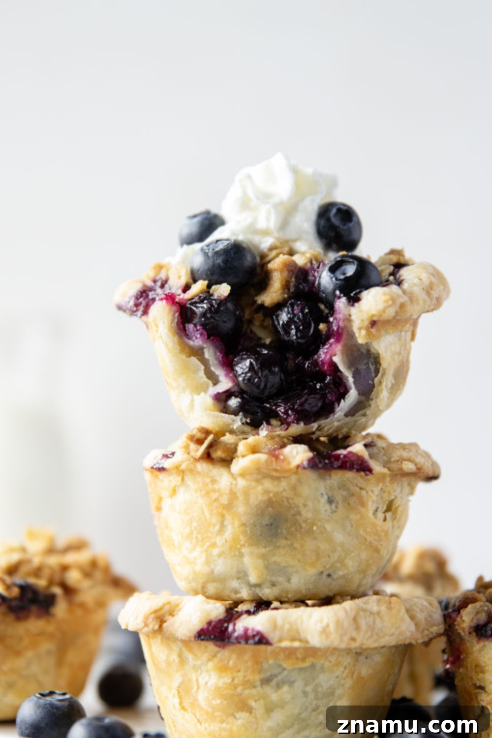 Oatmeal Cookie Streusel Blueberry Bites 6 A single mini blueberry tart, cut open to reveal the juicy blueberry filling and golden streusel, presented on a white plate.