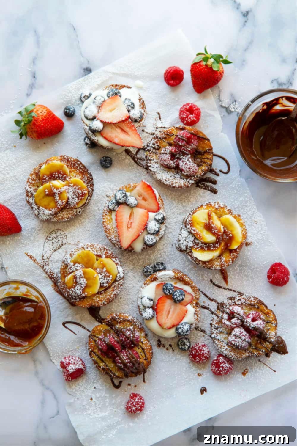 Mini Dutch Baby Bites 4 An array of Mini Dutch Baby Pancakes featuring three delicious toppings: melted chocolate with raspberries, caramel sauce with sliced banana, and whipped cream with mixed berries.